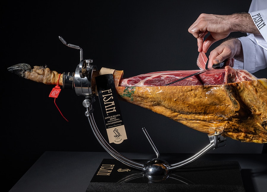 Jamonero con una pieza de jamón ibérico FISAN mientras una persona corta finas lonchas.