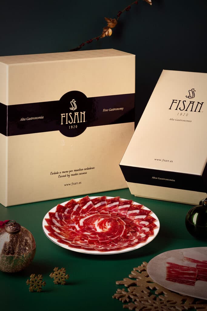 Plato de jamón ibérico loncheado frente a estuches de presentación de la marca FISAN