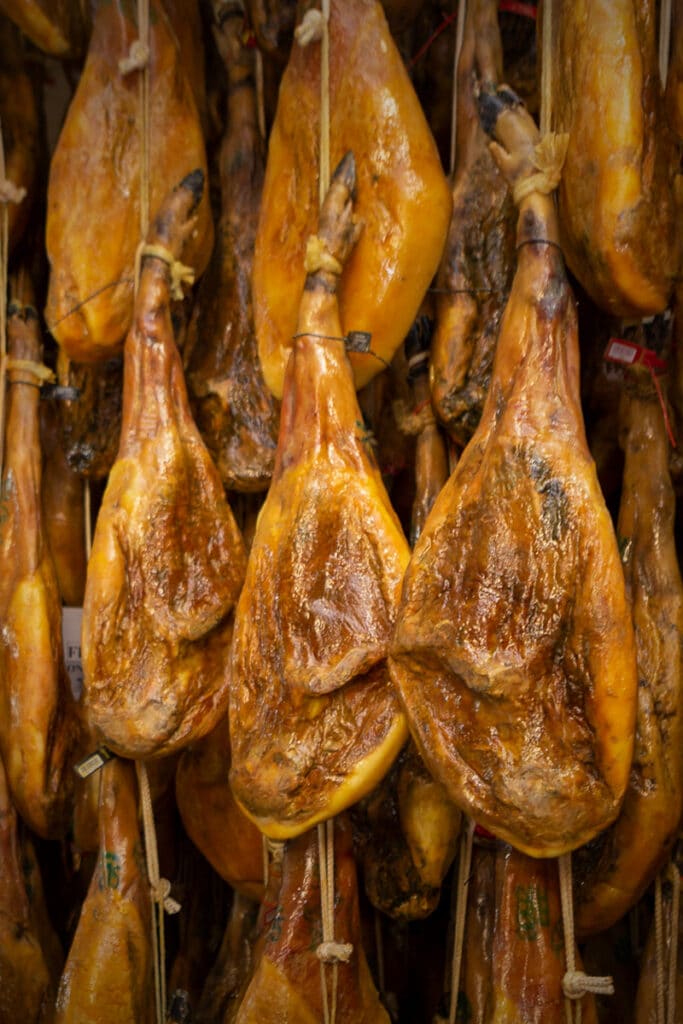 Primer plano de varias paletas y jamones ibéricos FISAN colgados en la bodega.