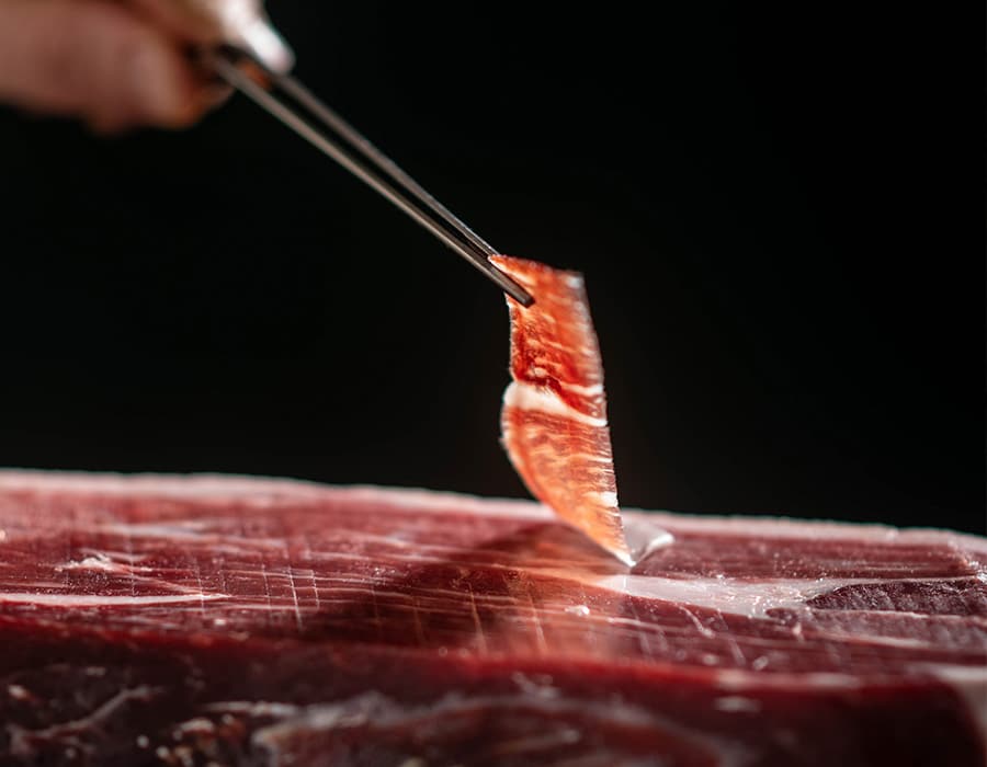 Primer plano de una loncha de jamón ibérico FISAN siendo cortada de una pieza entera.